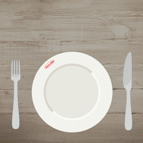 An empty plate between a fork and knife fills with chicken, grains, avocado and greens