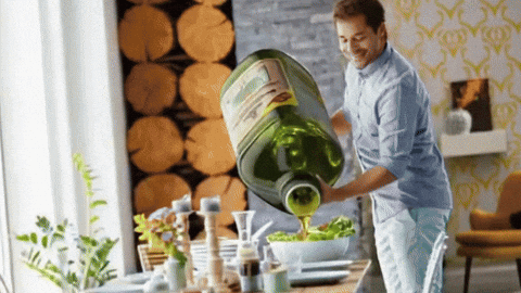 Olive oil poured from a bottle over a bowl of salad greens
