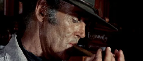 Henry Fonda coiffé d'un chapeau, fumant un cigare dans la pénombre