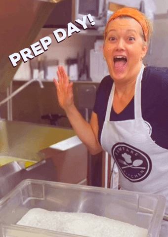 A cook in an apron in a kitchen cheering under the words Prep Day